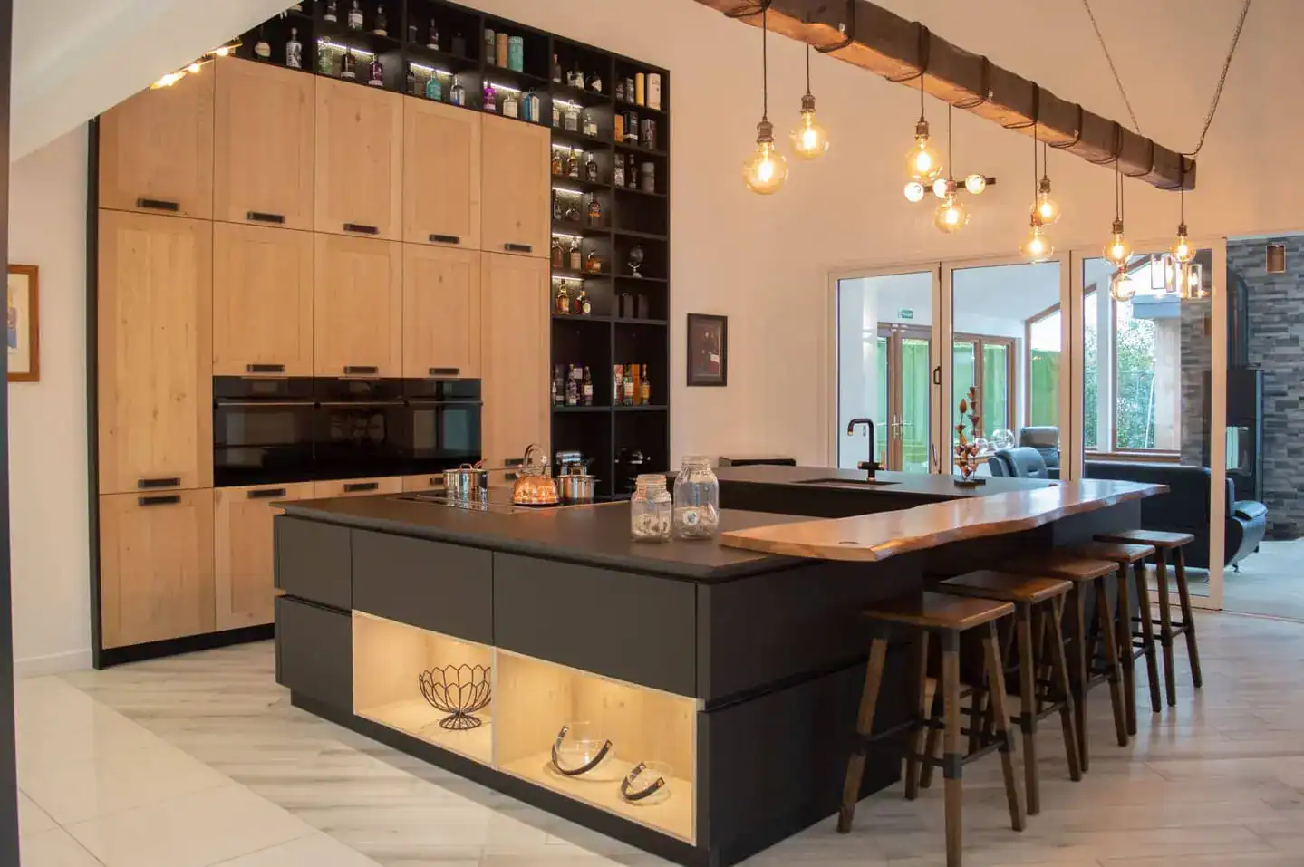 Contemporary showroom kitchen in Aberdeen, Scotland – black island with breakfast bar, warm pendant lights, light wood cabinetry, built-in ovens and open shelving