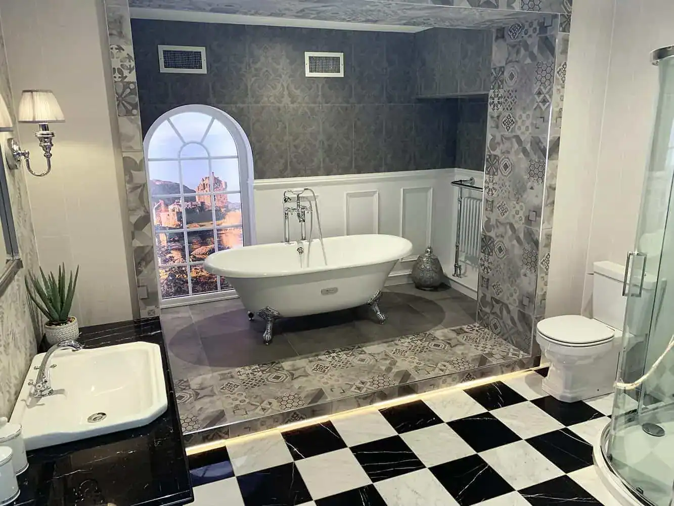 Modern luxury bathroom with freestanding clawfoot bath, patterned grey tiles, arched window, glass shower, toilet and black-and-white chequered floor