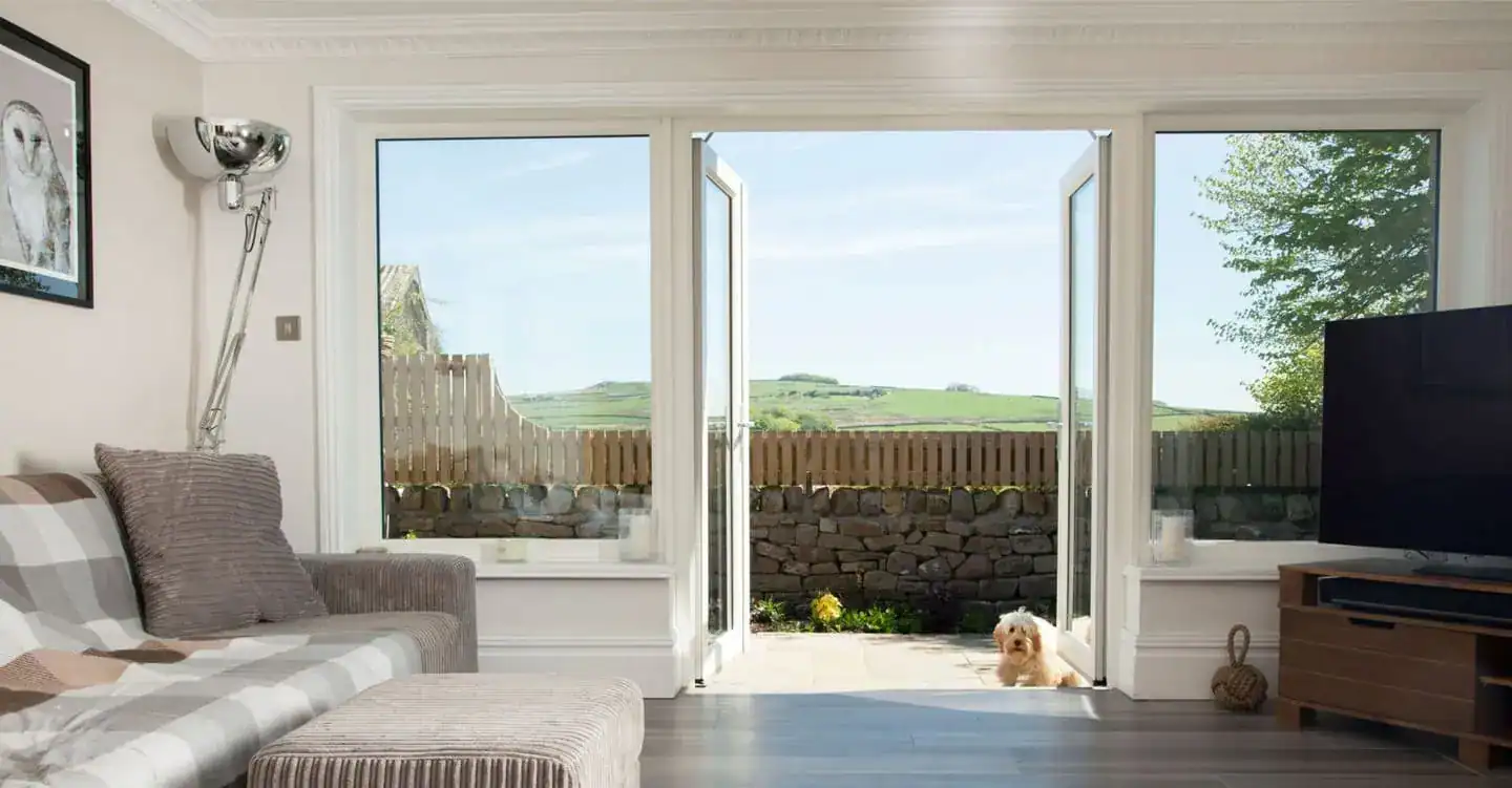 Bright living room with white French doors and large glazed panels opening onto a patio with countryside views.