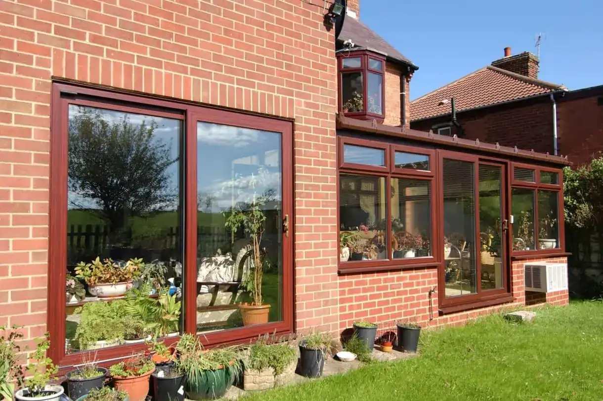 Sliding patio doors and large glazed windows with timber-effect frames on a brick home, opening onto a sunny garden.